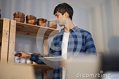An owner of vase brand checks online and physical inventory and maintains a diary record to determine product availability. A Stock Photo