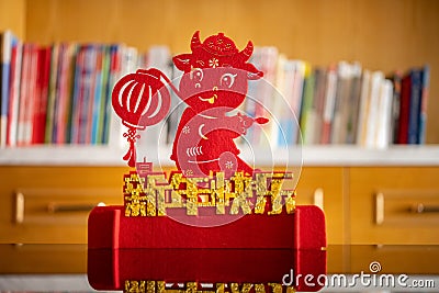 Ox mascot with lantern in front of a books shelf in a living room as symbol of Chinese New Year of the Ox 2021 translation of Stock Photo