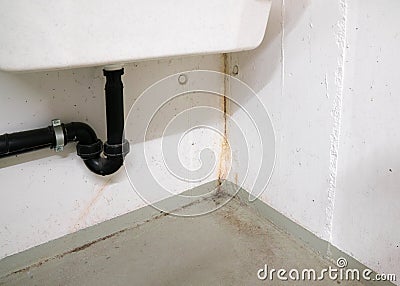 Oxidized and rusted calcium and mold and mildew deposits from water damage in a concrete cellar room under a large white sink Stock Photo