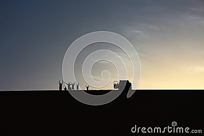 A pack of adventurers salute from the top of a grand sand dune while enjoying a beautiful summer sunset in Dakhla Oasis, Egypt Stock Photo