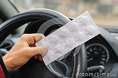 Pack of pills in the hands of the driver on a blurred background of the steering wheel in the car Stock Photo