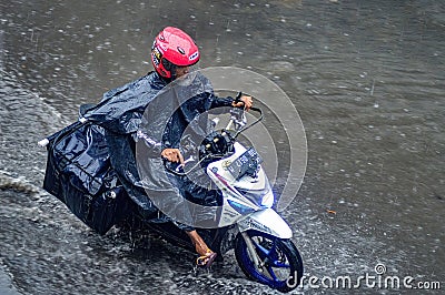a package courier who rides a motorbike who drives through flood waters during heavy rain in a residential area Editorial Stock Photo