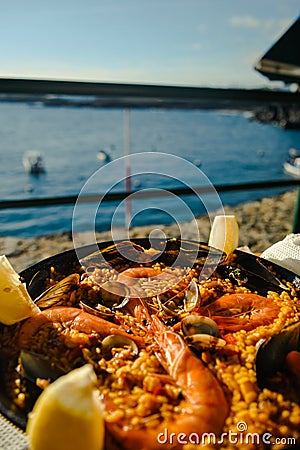 Paella with a huge iron spoon, shrimp and mussels, lemon. On the background of the sea in Spain in summer Stock Photo