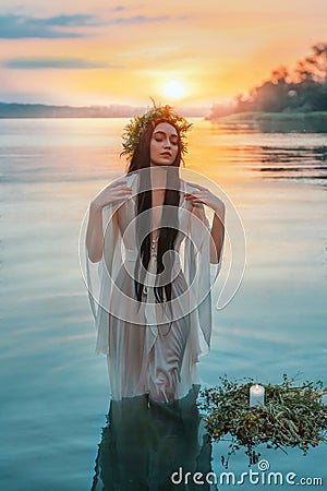 Pagan girl Slavic goddess emerges from water lake ritual flower wreaths float, candles burning. fashion model. Holiday Stock Photo
