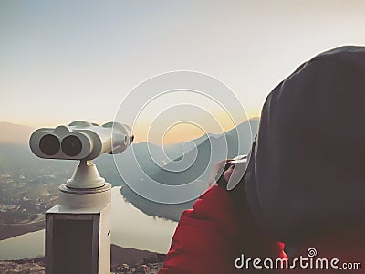 Paid outdoor tourist telescope. Girl in a red jacket taking pictures of the beautiful landscape Stock Photo