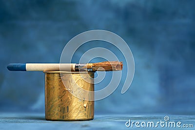 Paint brush on a tin can, painted in gold, on a blue textured background. Selective focus. Copy space Stock Photo
