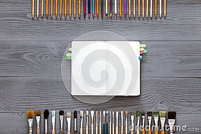 Paint brushes, color pencils and notebook on grey wooden background, art table. Top view with copy space Stock Photo