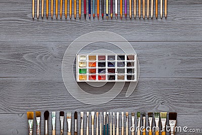 Paint brushes, color pencils and paintbox on grey wooden background, art table. Top view with copy space Stock Photo