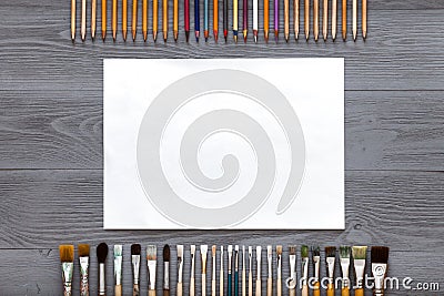 Paint brushes, color pencils and paper on grey wooden background, art table. Top view with copy space Stock Photo