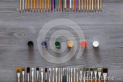 Paint brushes, color pencils and watercolors on grey wooden background, art table. Top view with copy space Stock Photo