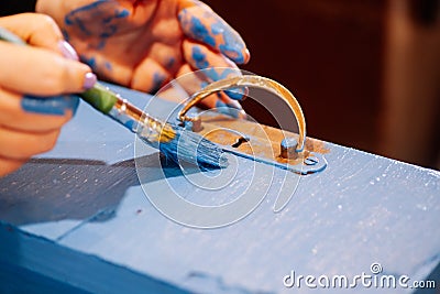 Paint-stained hands holding brush and painting antique wooden closet drawer in bright blue color. Reuse of old things Stock Photo