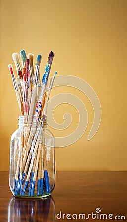 Paint stained paintbrushes in clear jar Stock Photo