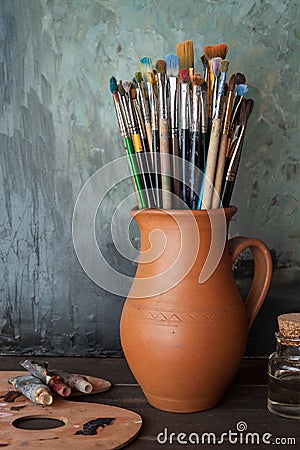 Paintbrushes in a jug from potters clay, palette and paint tubes Stock Photo