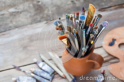 Paintbrushes in a jug from potters clay, palette and paint tubes Stock Photo