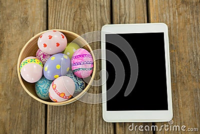 Painted Easter eggs in a bowl and digital tablet on wooden surface Stock Photo