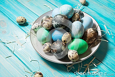 Painted eggs on plate, quail and chicken eggs, paint and brush on blue background, Easter decorations. Stock Photo