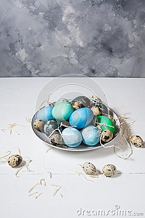 Painted eggs on plate, quail and chicken eggs, paint and brush on white wood background, Easter Stock Photo