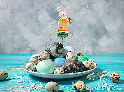 Painted eggs on plate, quail and chicken eggs, paint and brush on blue background, Easter decorations. Stock Photo