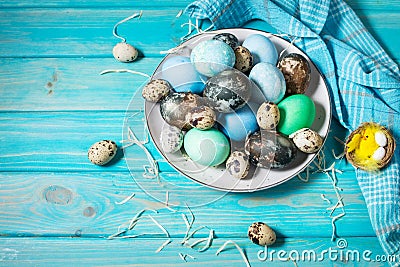Painted eggs on plate, quail and chicken eggs, paint and brush on blue background, Easter decorations. Stock Photo