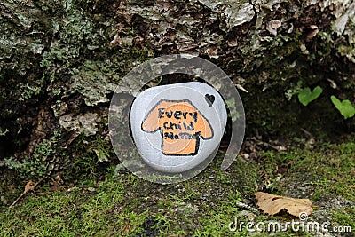 A painted rock at the base of a tree along a trail in Nova Scotia orange shirt every child matters Stock Photo