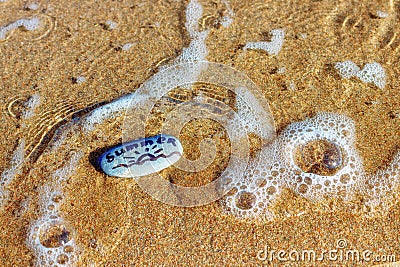 Painted sea pebbles on a summer beach in the oncoming wave. Stock Photo