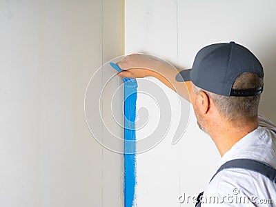 The painter applies blue paint with a brush on the wall Stock Photo