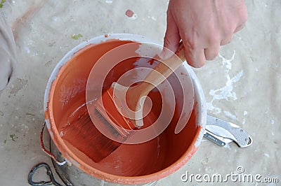 Painter Applies Orange Paint to Brush from Pail Stock Photo
