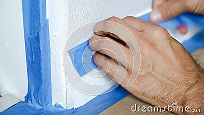 Painter Man Using Masking Blue Tape to Secure Baseboard, Moulding Stock Photo