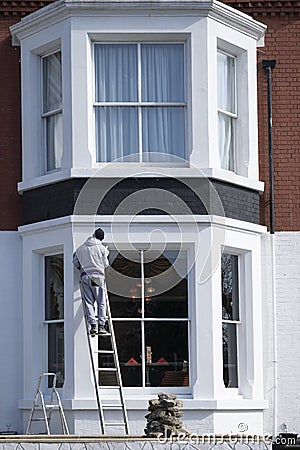 Painter on top of ladder painting white the facade of Pearl Hotel in Peterborough with perspective from down up. Editorial Stock Photo