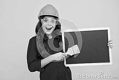 Painter in workshop. Renovation and repair. Teen girl in helmet with painting brush. Child in hard hat. Kid builder Stock Photo