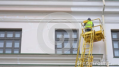 Painters standing on Aerial ladder paint the wall on construction site Stock Photo