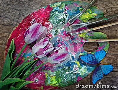Painting concept. artist`s palette and brushes, tulip flowers and colorful blue morpho butterfly on a wooden table. Stock Photo