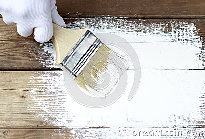 Painting a wooden surface with white paint, a gloved hand holding a paint brush Stock Photo