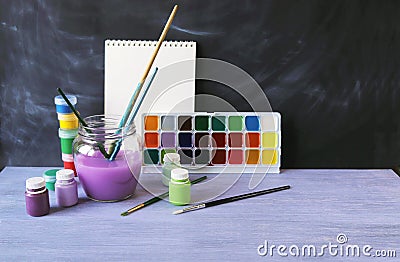 Paints, brushes, water on a wooden table against the background of a chalkboard Stock Photo