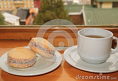 Pair of Alfajores, Traditional Latin American Sweets and a Cup of Hot Tea Served on Wooden Table by the Window, Ushuaia Stock Photo