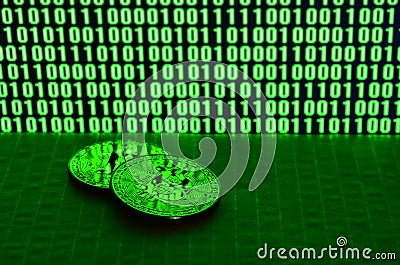 A pair of bitcoins lies on a cardboard surface on the background of a monitor depicting a binary code of bright green zeros and on Stock Photo
