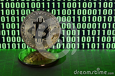 A pair of bitcoins lies on a cardboard surface on the background of a monitor depicting a binary code of bright green zeros and on Stock Photo
