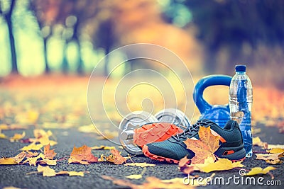 Pair of blue sport shoes water and dumbbells laid on a path in a tree autumn alley with maple leaves - accessories for run exerc Stock Photo