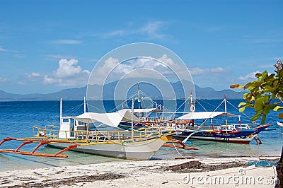 A pair of boats sit in the crystal clear blue waters off the coast of the Philippines with gorgeous mountains and blue sky Editorial Stock Photo