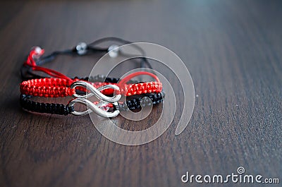 Pair bracelets in black and red with infinity. Handmade woven bracelets. Handmade decorations. Background with beads with hearts Stock Photo