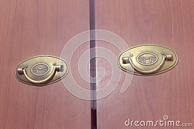 Pair of brass folding pull handles on wooden doors of wardrobe Stock Photo