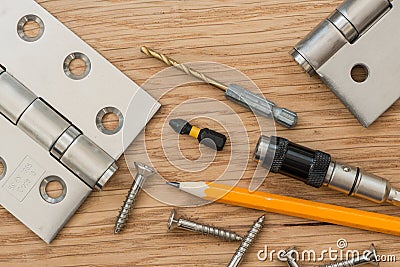 A pair of brushed steel door hinges and tools, on wooden surface Stock Photo