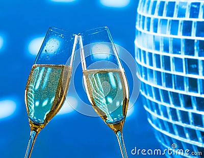 A pair of champagne flutes with golden bubbles make cheers on sparkling blue disco ball background Stock Photo