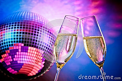 A pair of champagne flutes with golden bubbles make cheers on sparkling blue and violet disco ball background Stock Photo