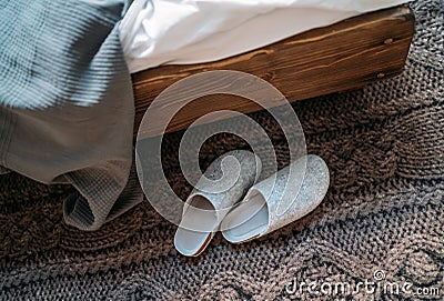 The pair of gray home slippers near the wooden bed on the Stock Photo