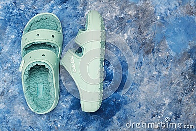 pair of green Crocs sandals with faux fur on blue background. View from above. Space for text Editorial Stock Photo