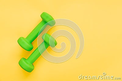 Pair of green feminine dumbbells on yellow background. Healthy lifestyle, body slimming concept. Empty space for text. Stock Photo