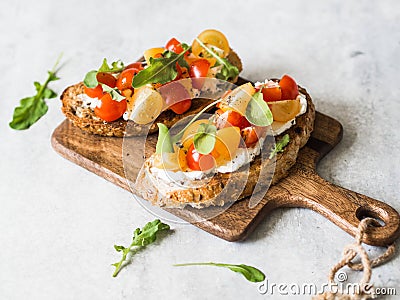 Pair of grilled toasts with cream cheese and slices of fresh tomatoes of various colors with fresh arugula and ground black pepper Stock Photo