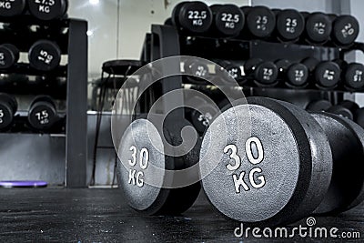 A pair of 30 kilo dumbbells on the floor with a dumbbell rack at the background. Stock Photo