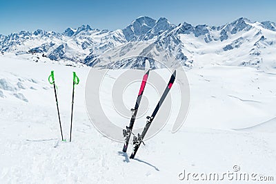 A pair of skis and ski poles stick out in the snow on the mountain slope of the Caucasus against the backdrop of the Stock Photo